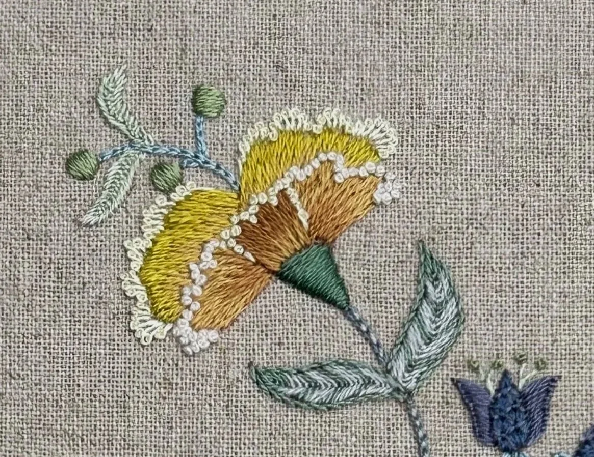 Detail of silk embroidered flower. Long and short stitch petals with knots along the edges.