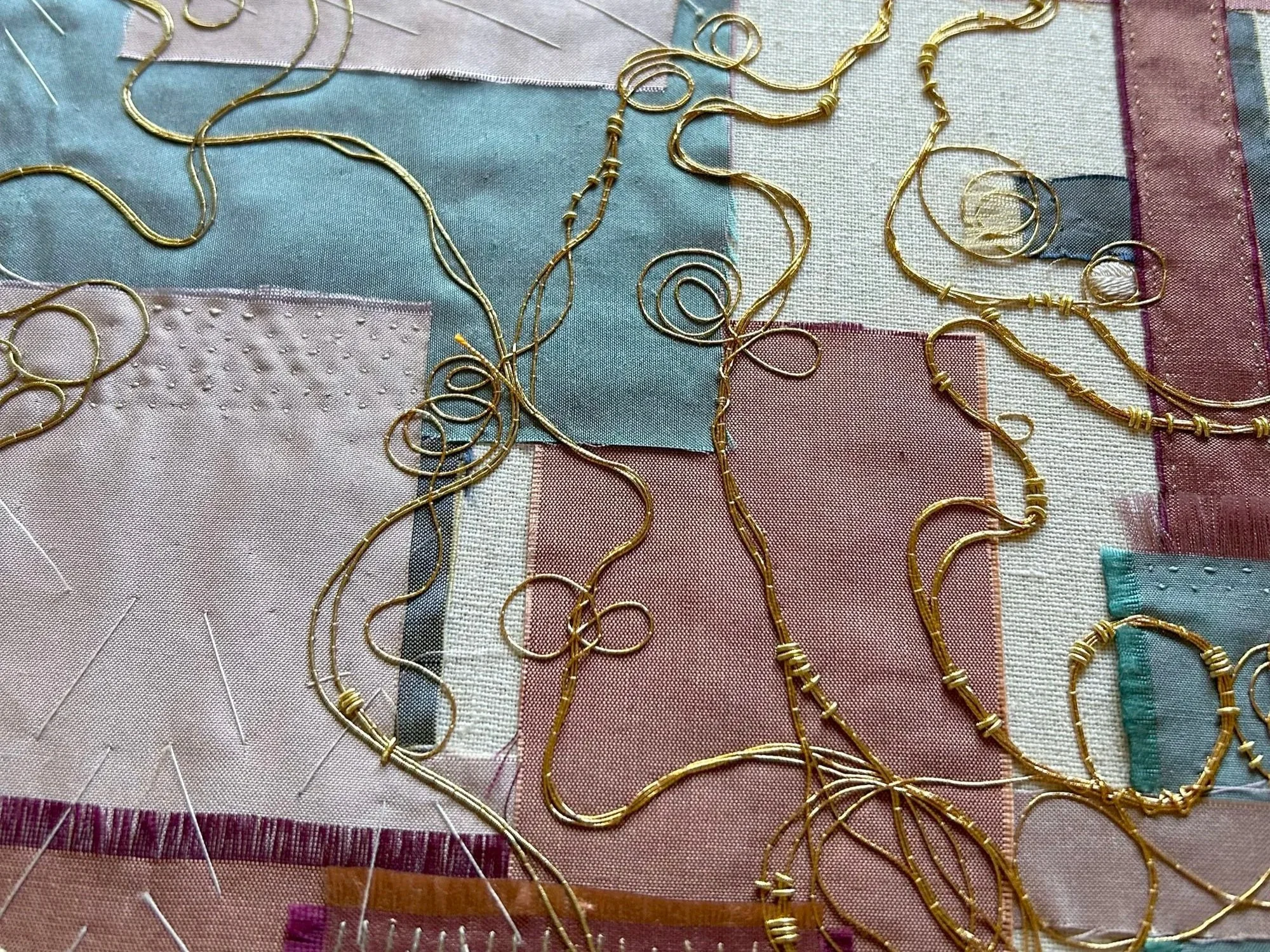 Creative goldwork embroidery . Layered silk fabrics in shades fo pink and blue with gold metal threads stitched in place in a coiling pattern by Anna Scott.
