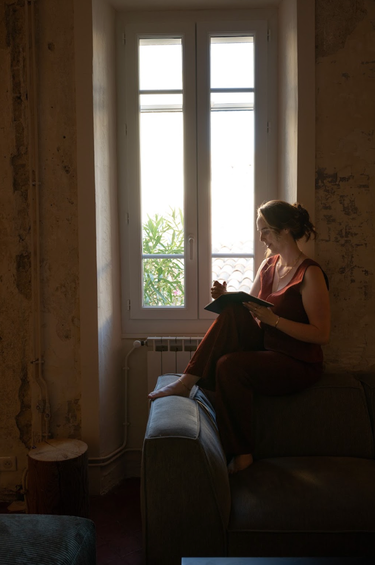 Thought leadership architect Emily M. Walker reading and writing in a book while relaxing on a sofa beside a large window.