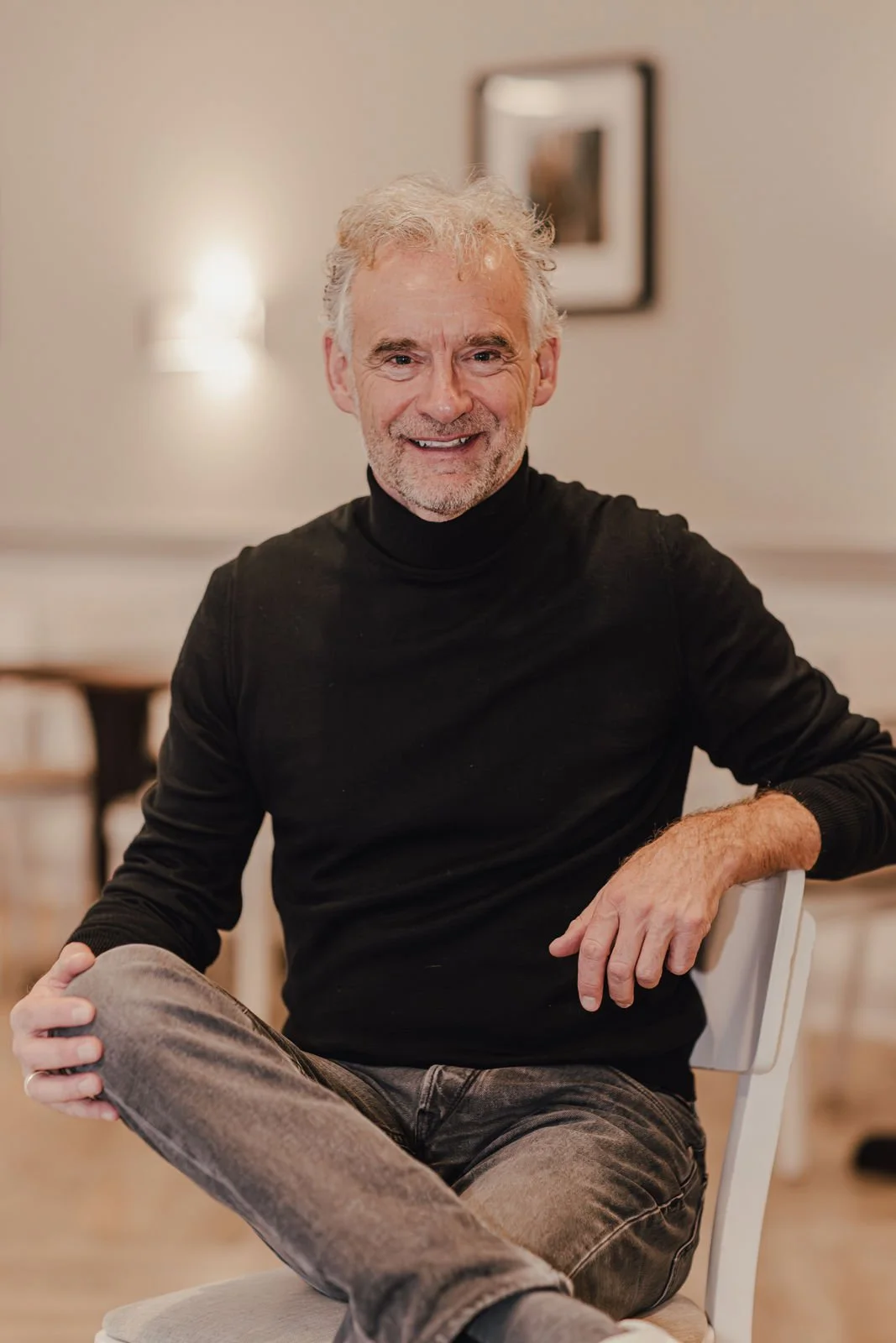 Ein Mann mit grauem Bart und blauen Hemd steht vor einer Solaranlage unter klarem blauen Himmel.