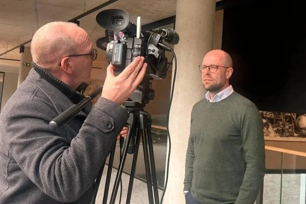 een man wordt gefilmd door een cameraman in een binnenruimte.