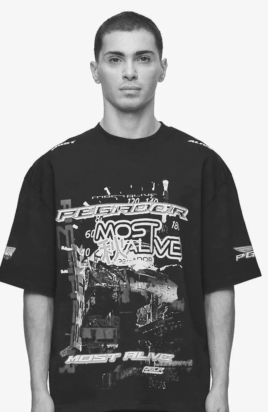 A young man with short hair wearing a graphic T-shirt standing against a plain background.