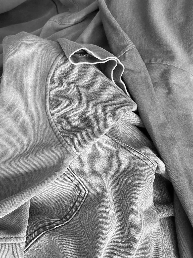 A close-up image of several folded and layered gray clothing items with different textures and stitching visible.