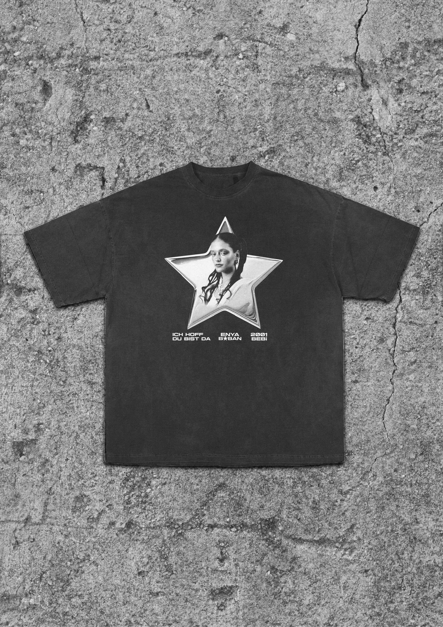 Black T-shirt with a black and white graphic of a woman's portrait inside a star and German text beneath on a cracked concrete surface.