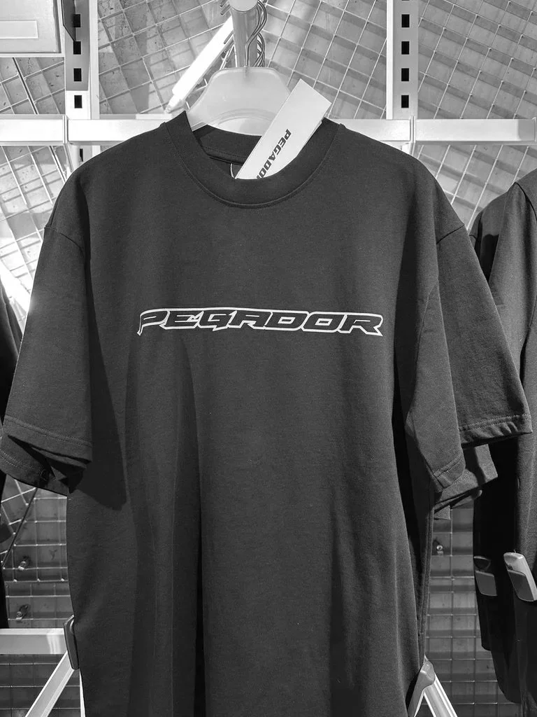 Black T-shirt with 'PEGRADOR' logo hanging on a store rack.