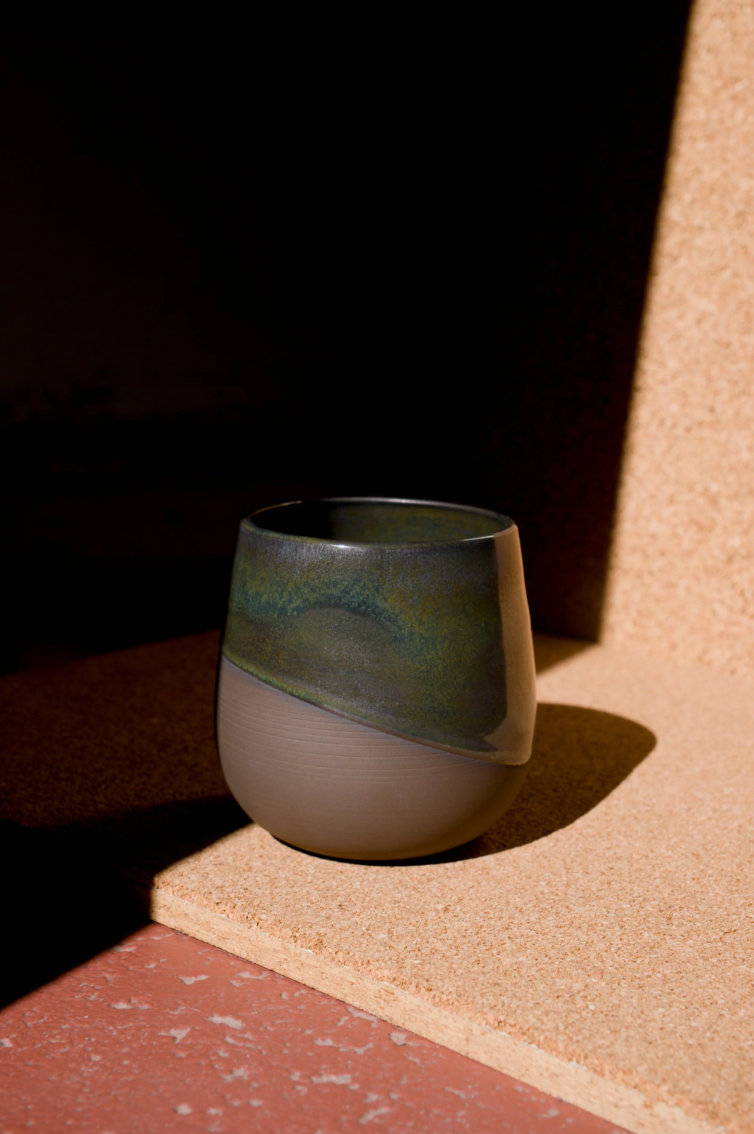 Un verre à bière en céramique avec design moderne and colorée, placée sur une surface de liège, créant un contraste avec le fond sombre et la lumière qui met en valeur ses détails de surface et ses couleurs.
