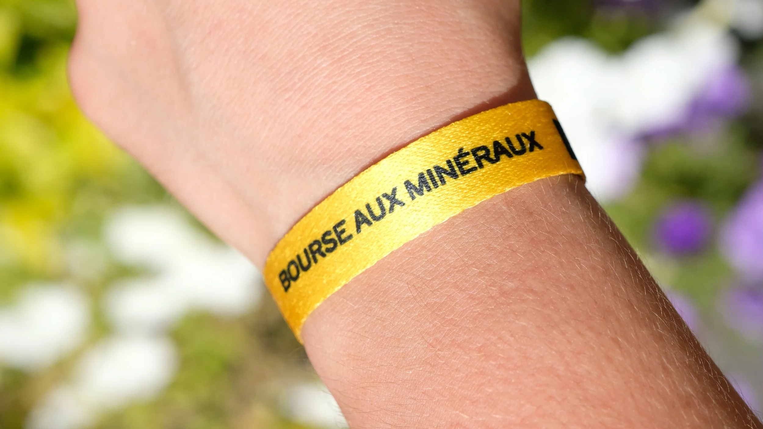 Poignet portant un bracelet jaune avec le texte 'BOURSE AUX MINÉRAUX' en noir.