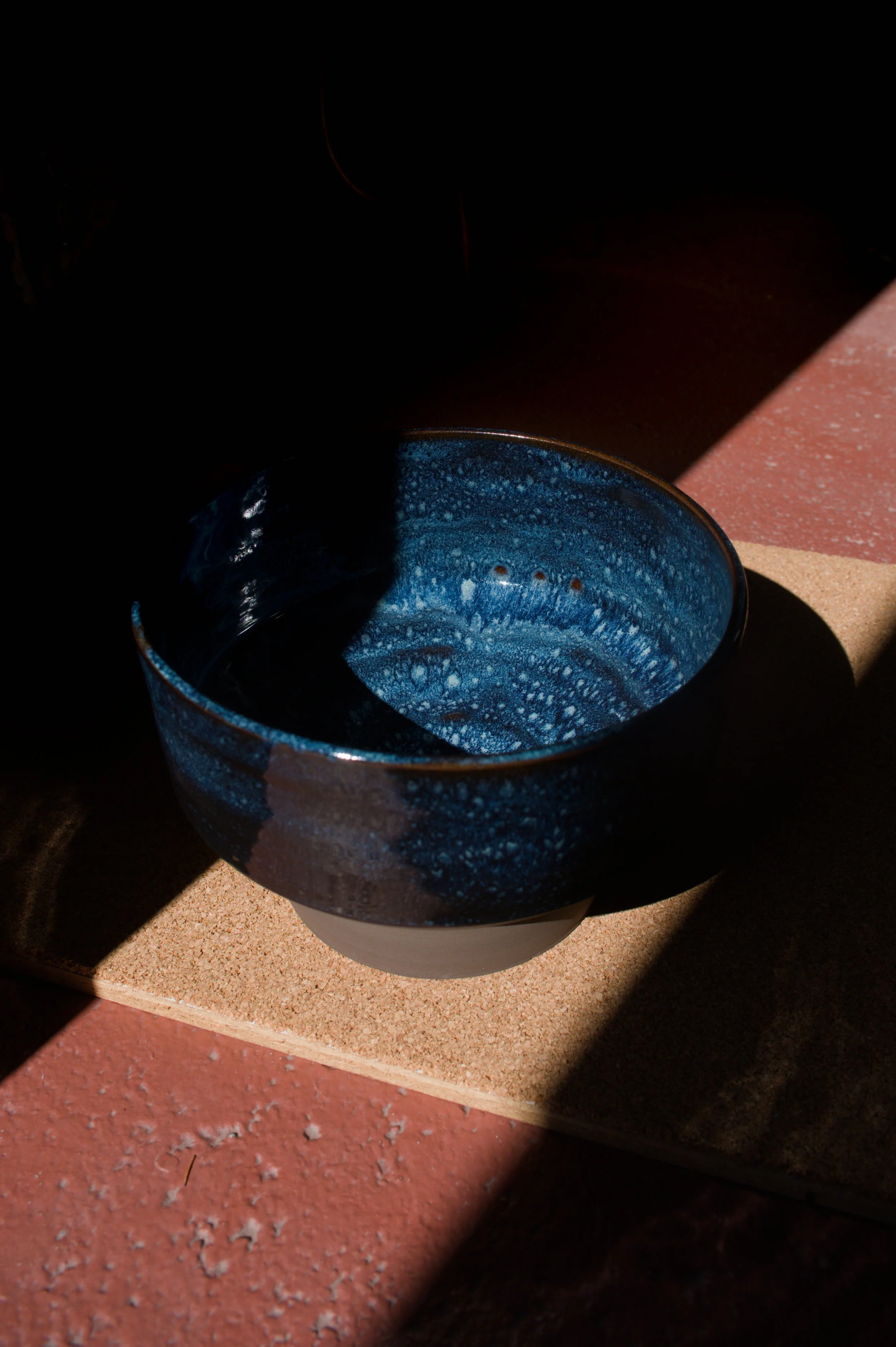 Un bol en céramique bleu foncé avec un intérieur bleu, posée sur une base en liège, sur un sol en rouge. 