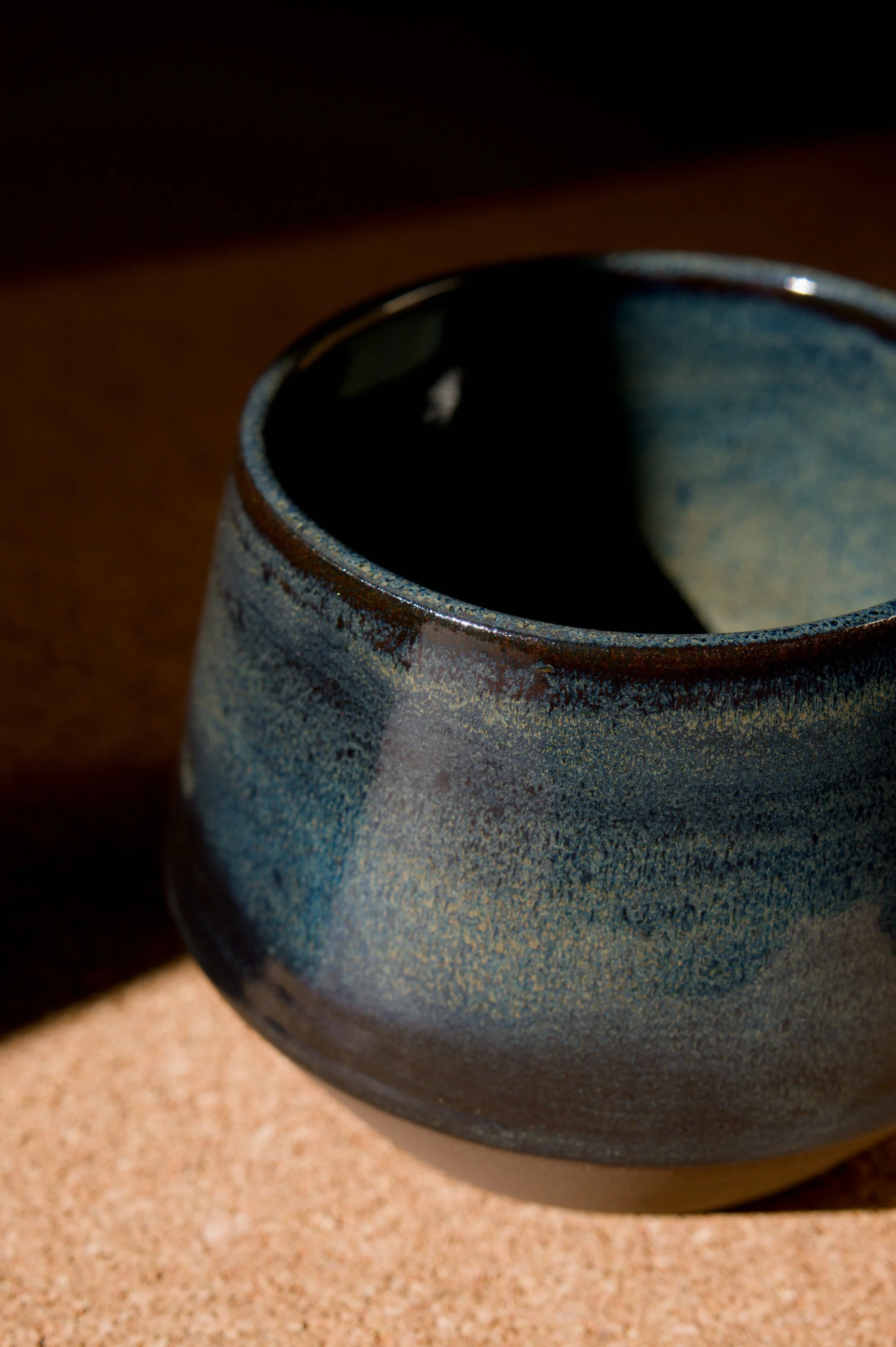 Une tasse en céramique bleue avec un intérieur noir, posée sur une surface en liège.