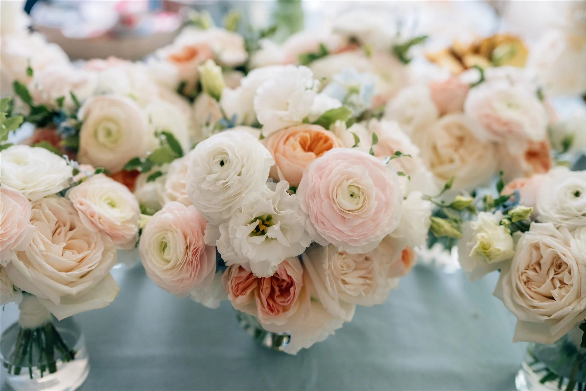 A bouquet of soft pink and white roses and ranunculus flowers arranged in vases.