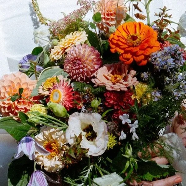 A colorful bouquet of various flowers including orange, pink, purple, and white blooms, with green foliage.