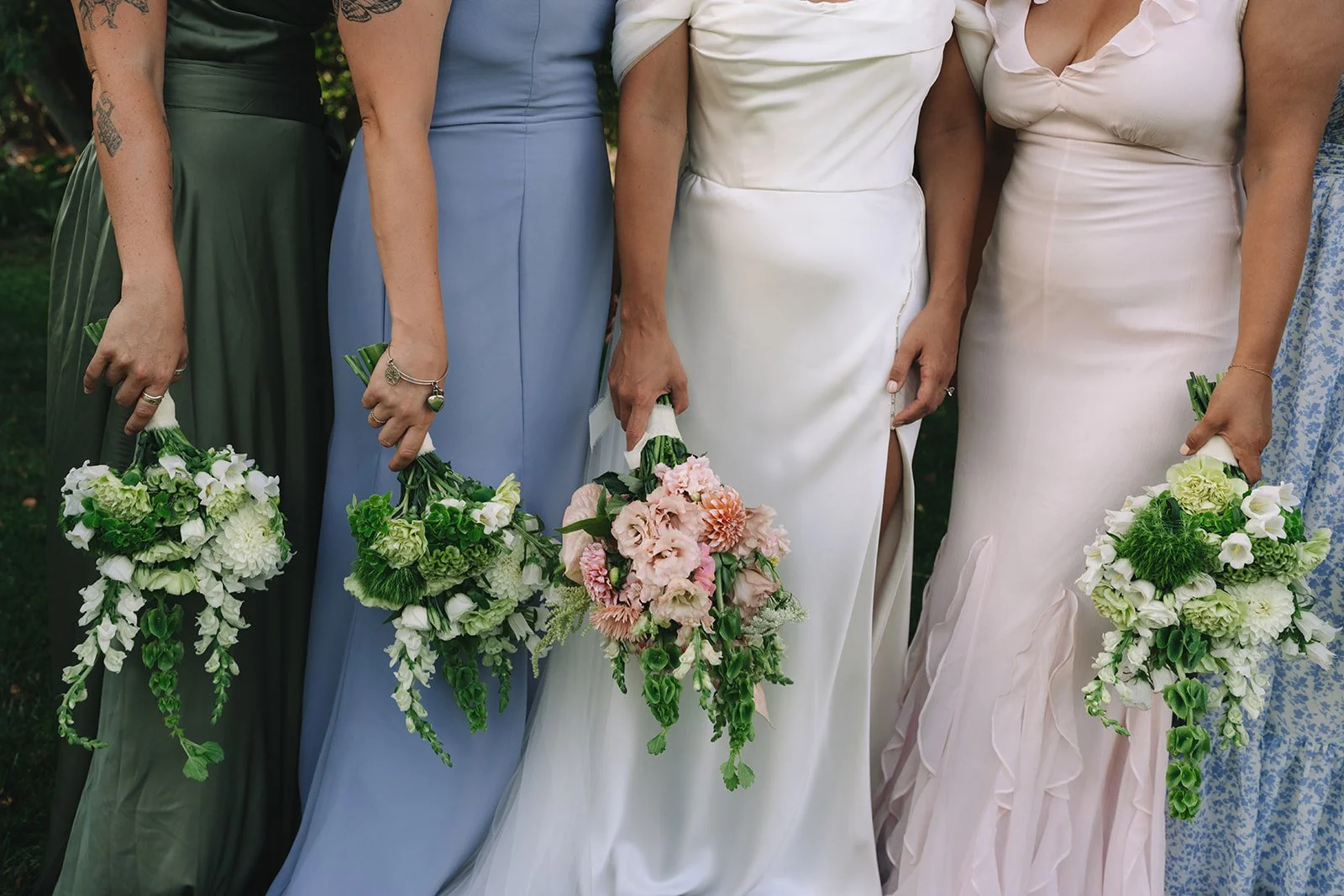 A group of women in colorful dresses holding bouquets of flowers, standing outdoors.