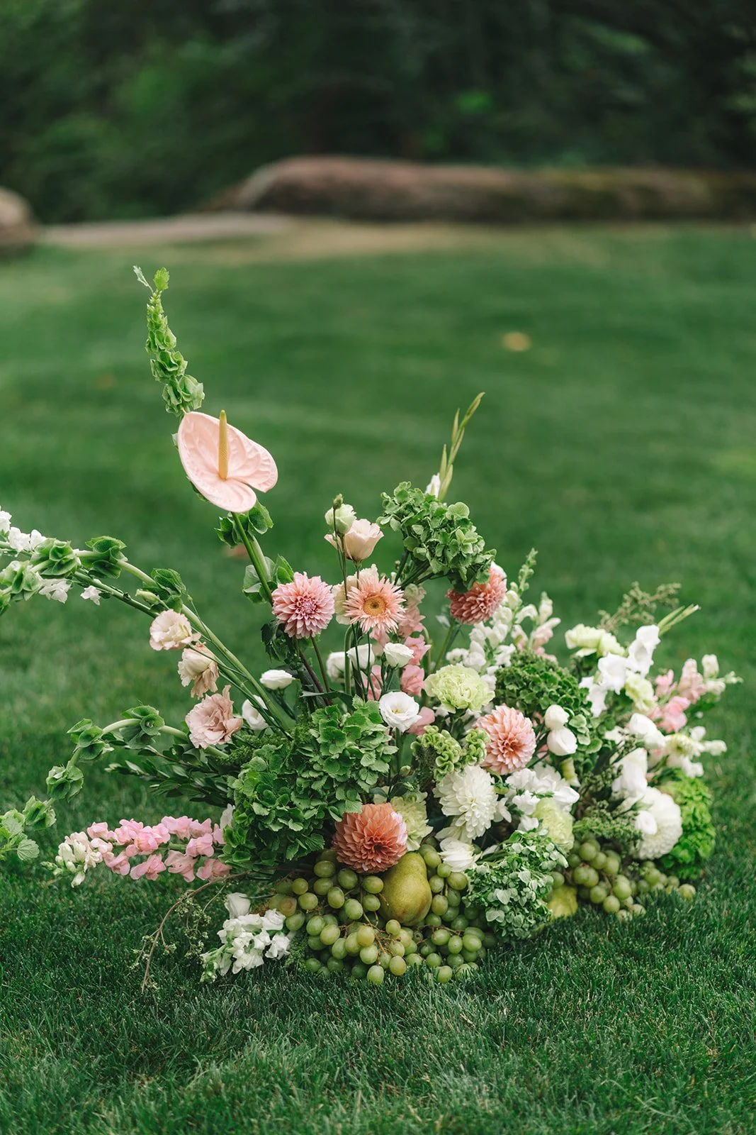 A large bouquet of pink, white, and green flowers on green grass with blurred greenery background.