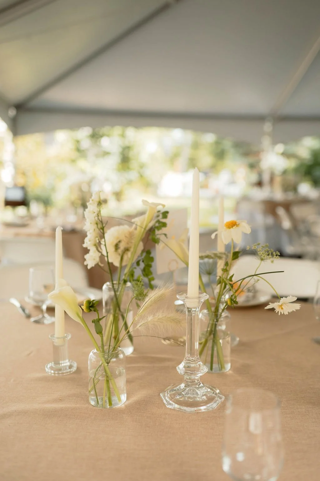 Elegant table centerpiece with white flowers and candles in a glass holder at an outdoor event.