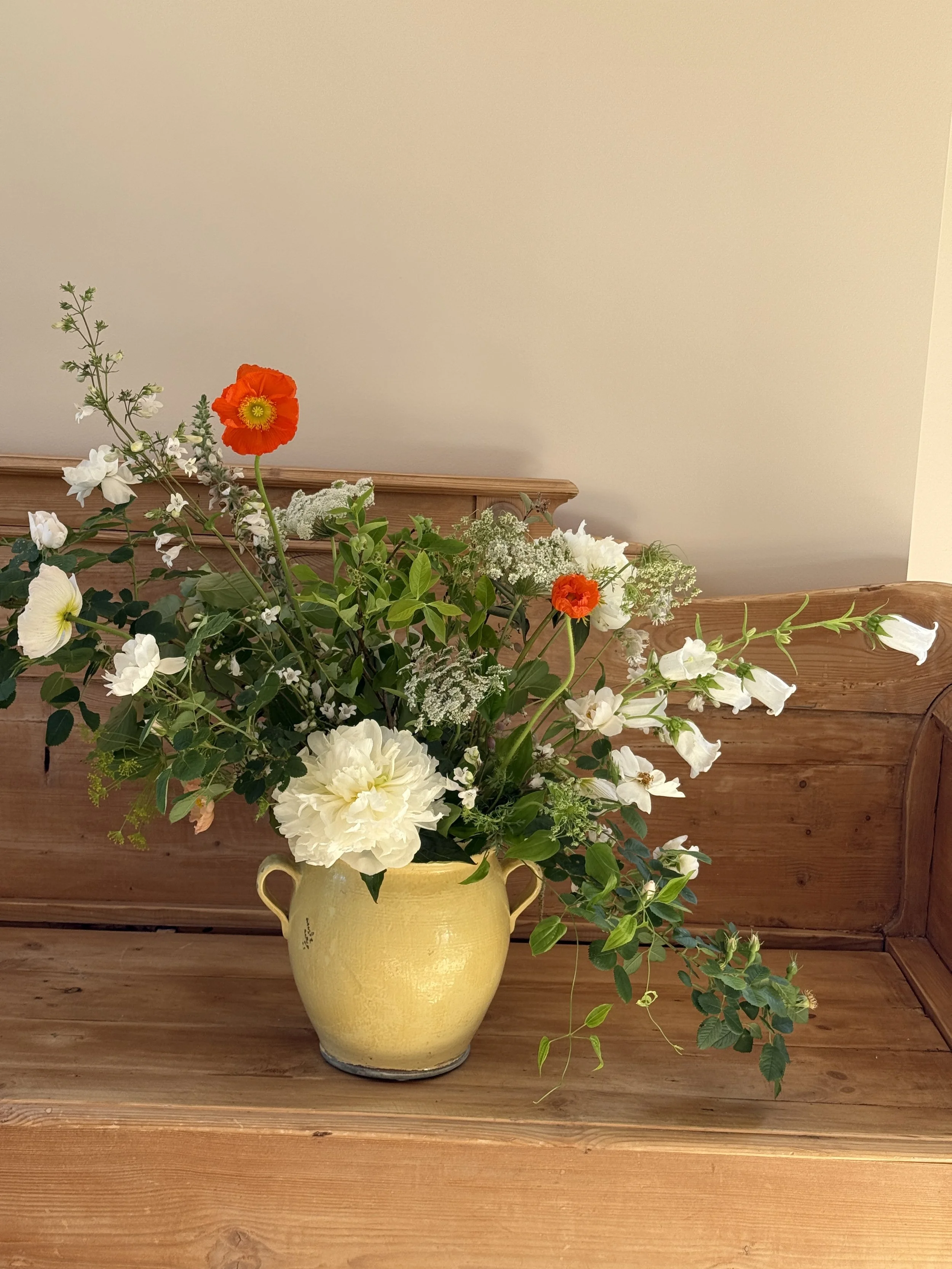 A yellow ceramic vase with a bouquet of white, orange, and green flowers placed on a wooden surface.