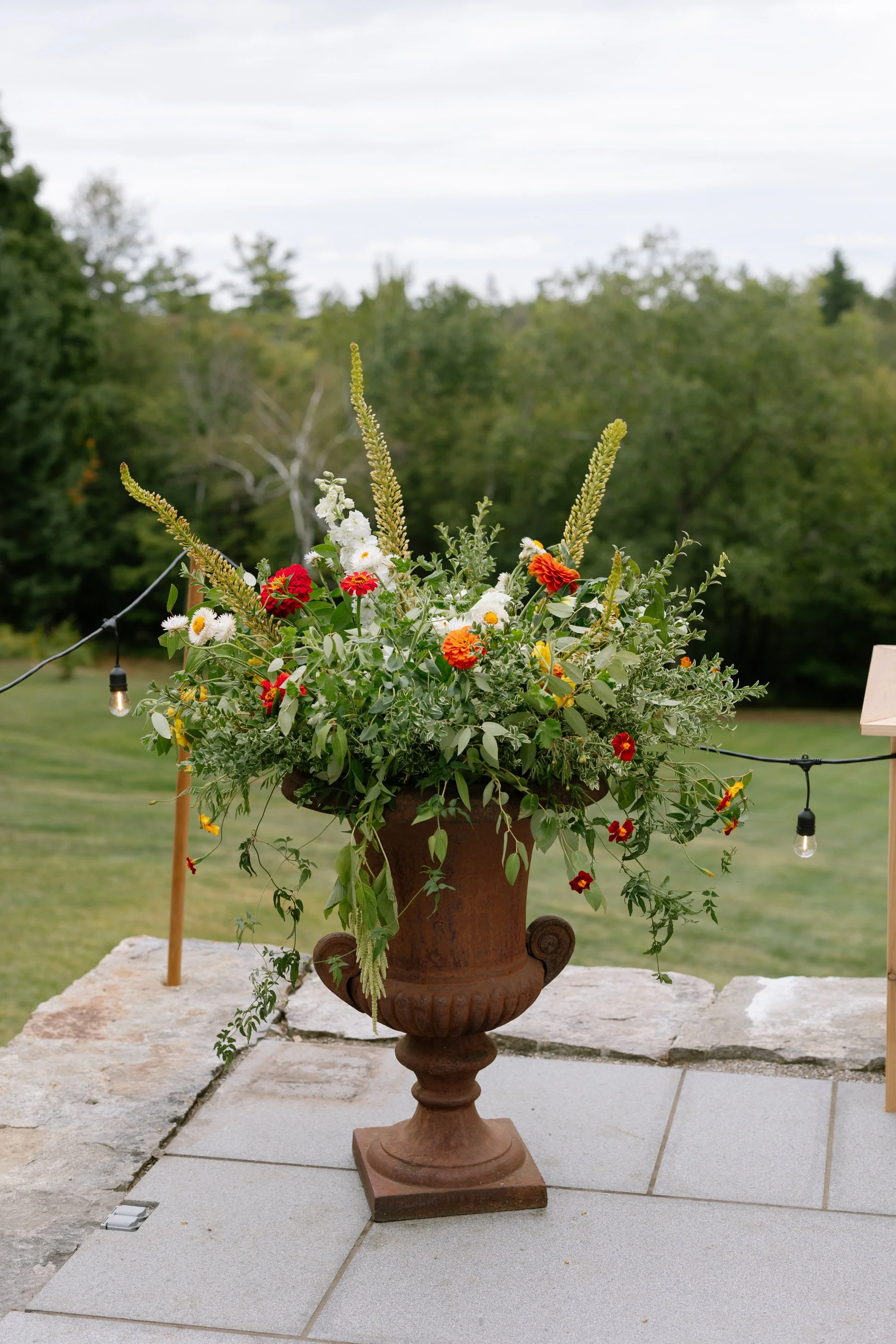 A large terracotta vase filled with a colorful arrangement of flowers and greenery on a stone patio outdoors.