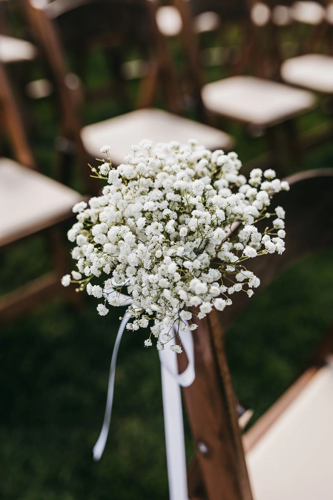 White baby's breath flowers tied to a wooden chair at an outdoor wedding ceremony.