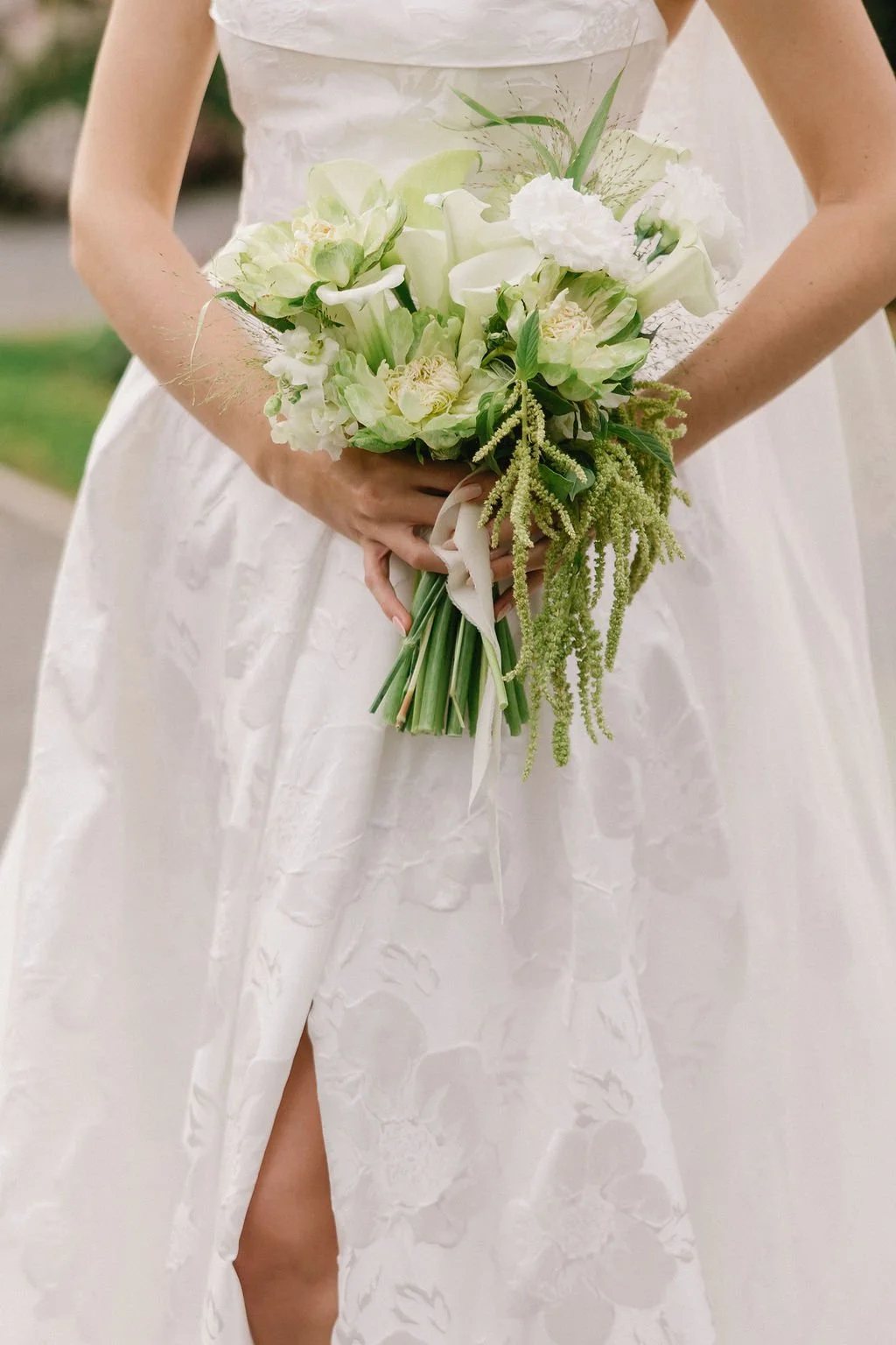 Bride holding a white-green floral bouquet in a white dress with a slit.