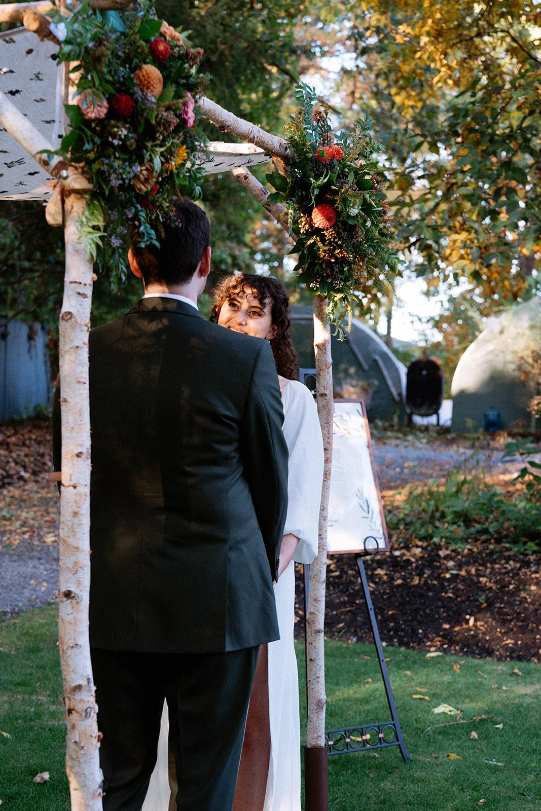 A couple getting married outdoors under a rustic wooden arch decorated with colorful flowers and greenery.