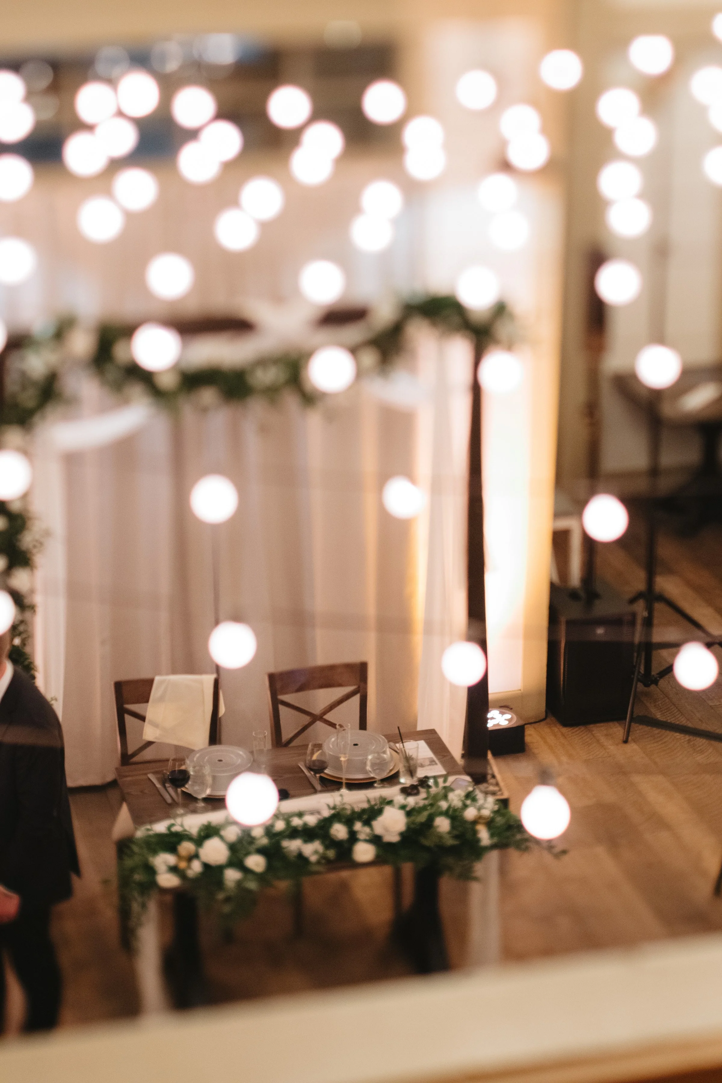 Wedding or event reception area decorated with string lights and floral arrangements on a table.