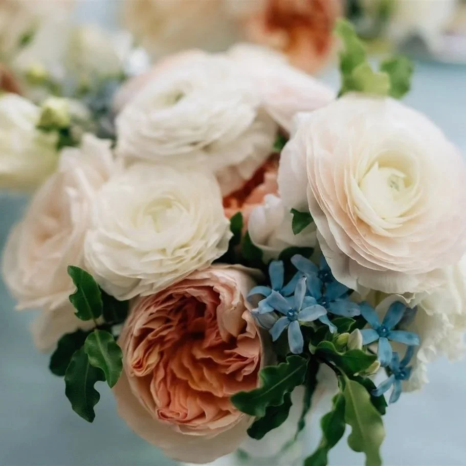 Close-up of a bouquet of white and peach roses with green leaves and small blue flowers.