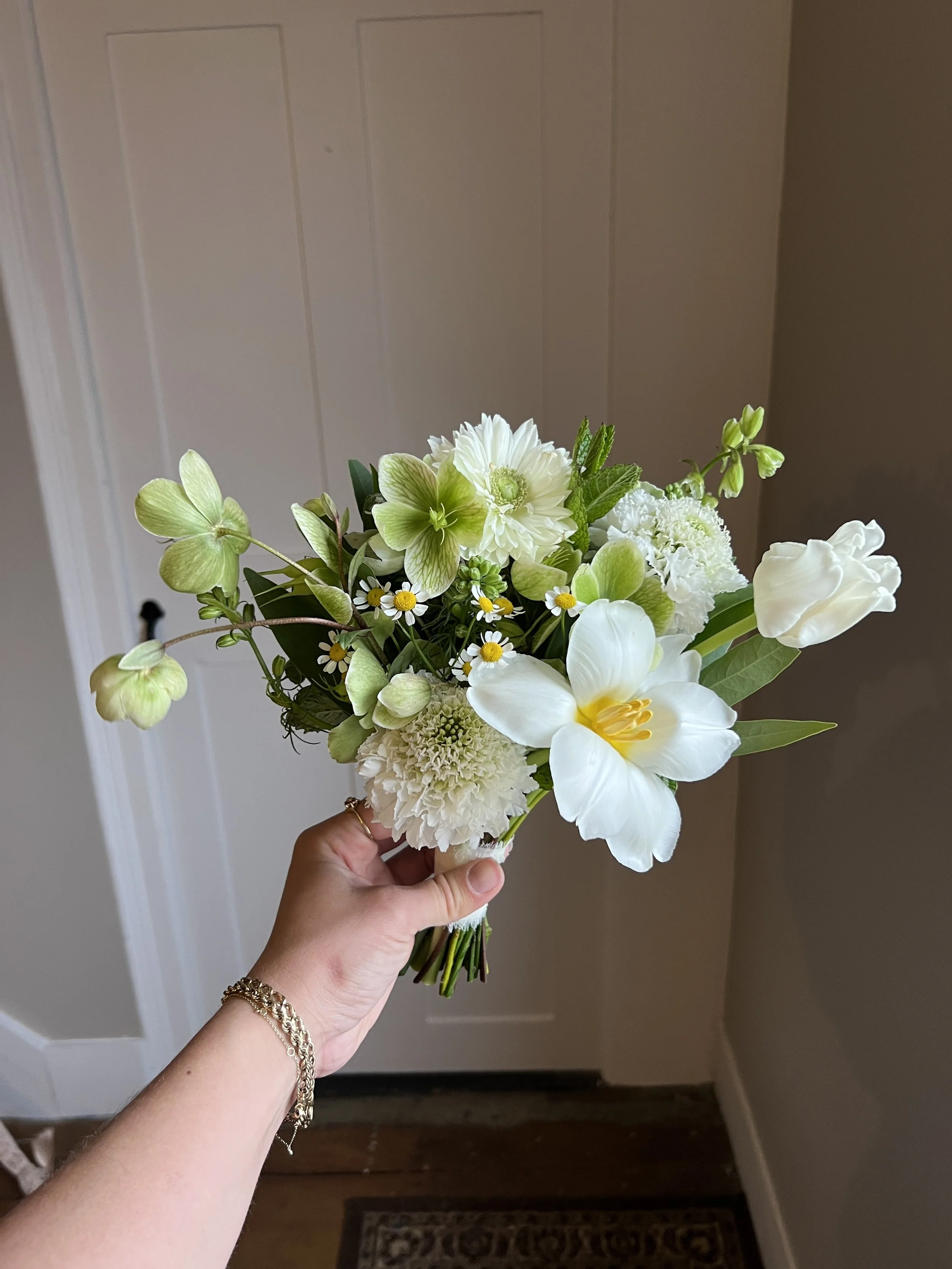 Hand holding a bouquet of white and green flowers
