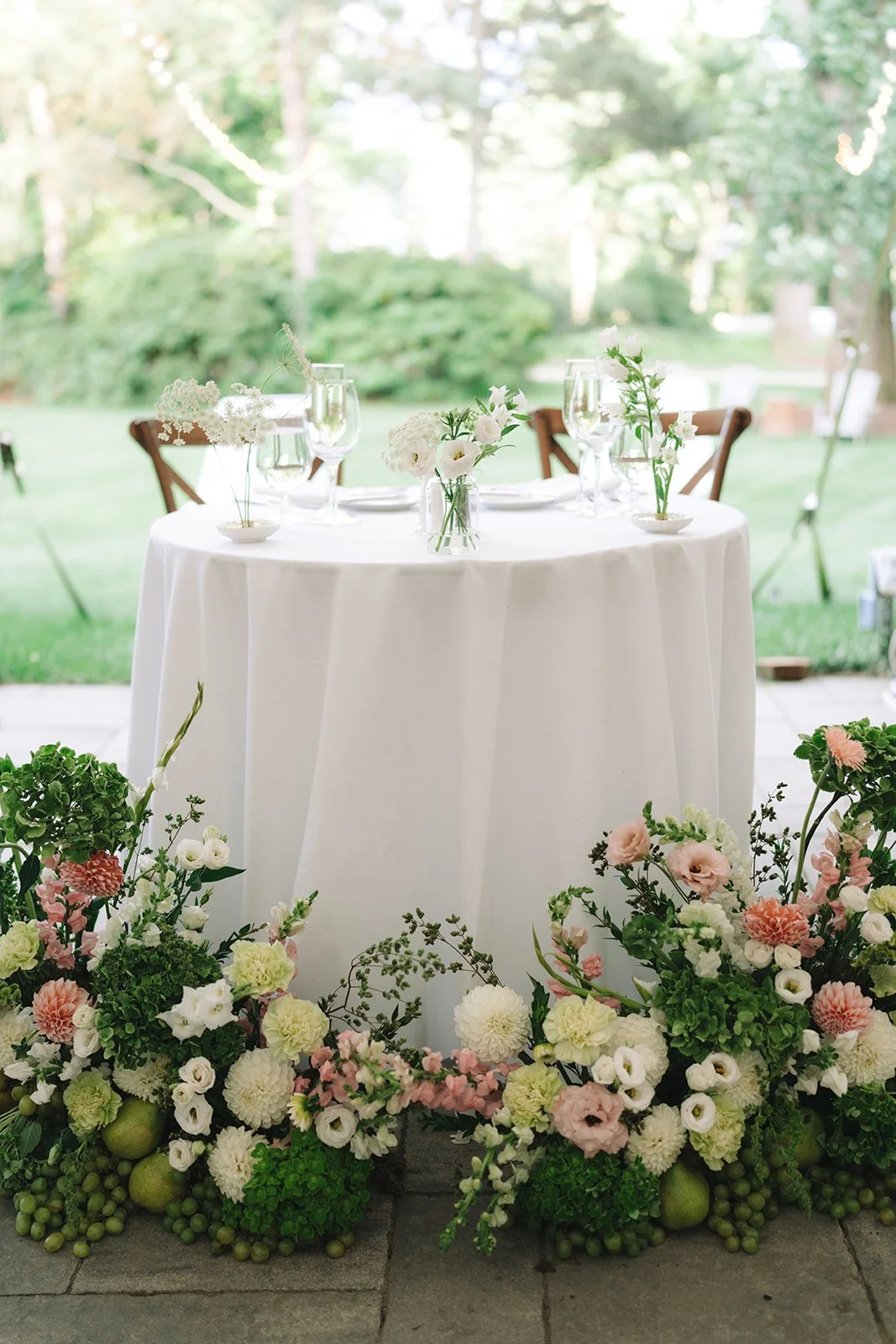 Elegant outdoor wedding reception table decorated with white flowers and surrounded by lush greenery.