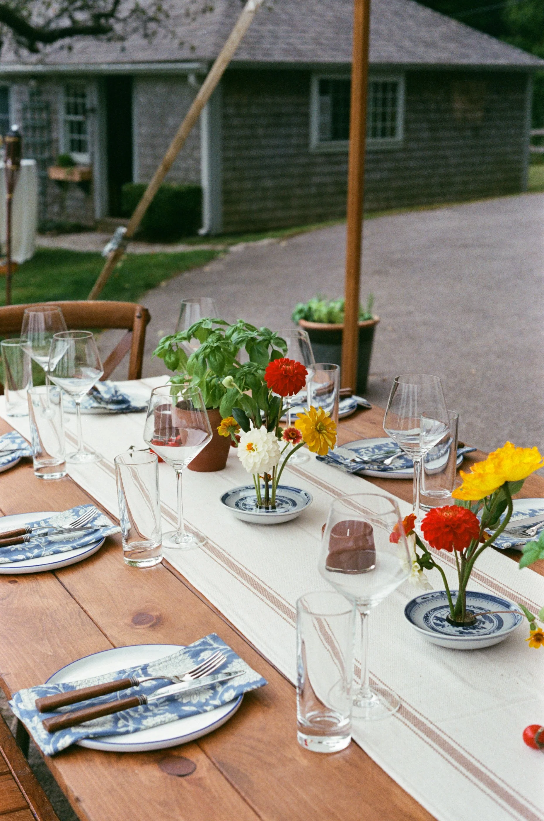 Outdoor dining table set with plates, utensils, glasses, and colorful flowers in the center.