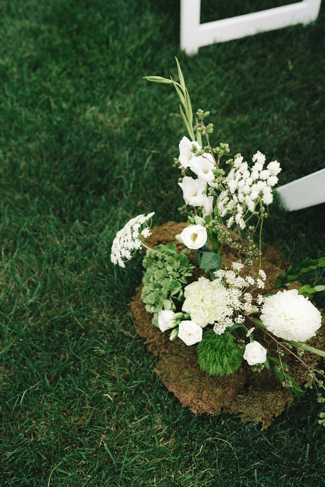 White floral arrangement with various flowers and greenery on a grassy area.