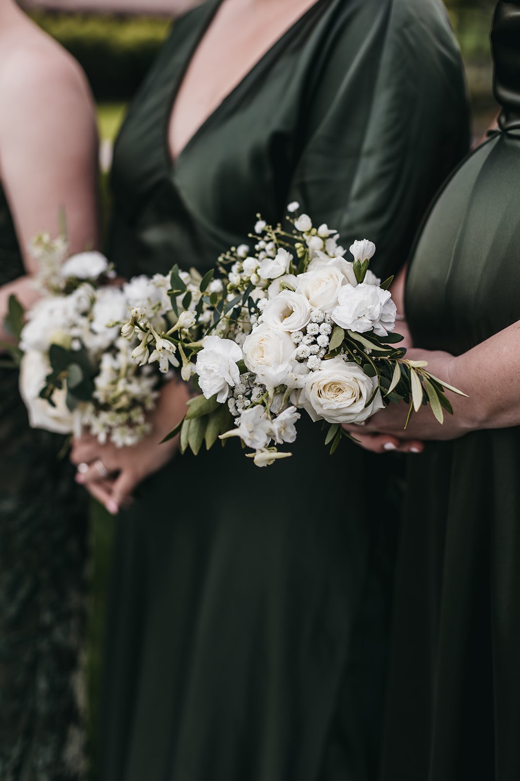 Women wearing dark green dresses holding white floral bouquets at an outdoor event.