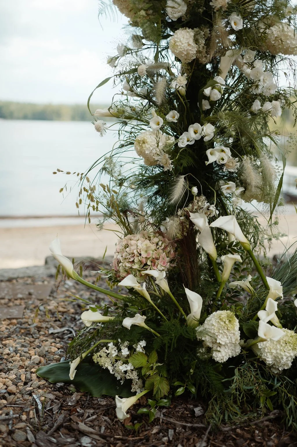 White floral arrangement by a lakeside with water and sky in the background.