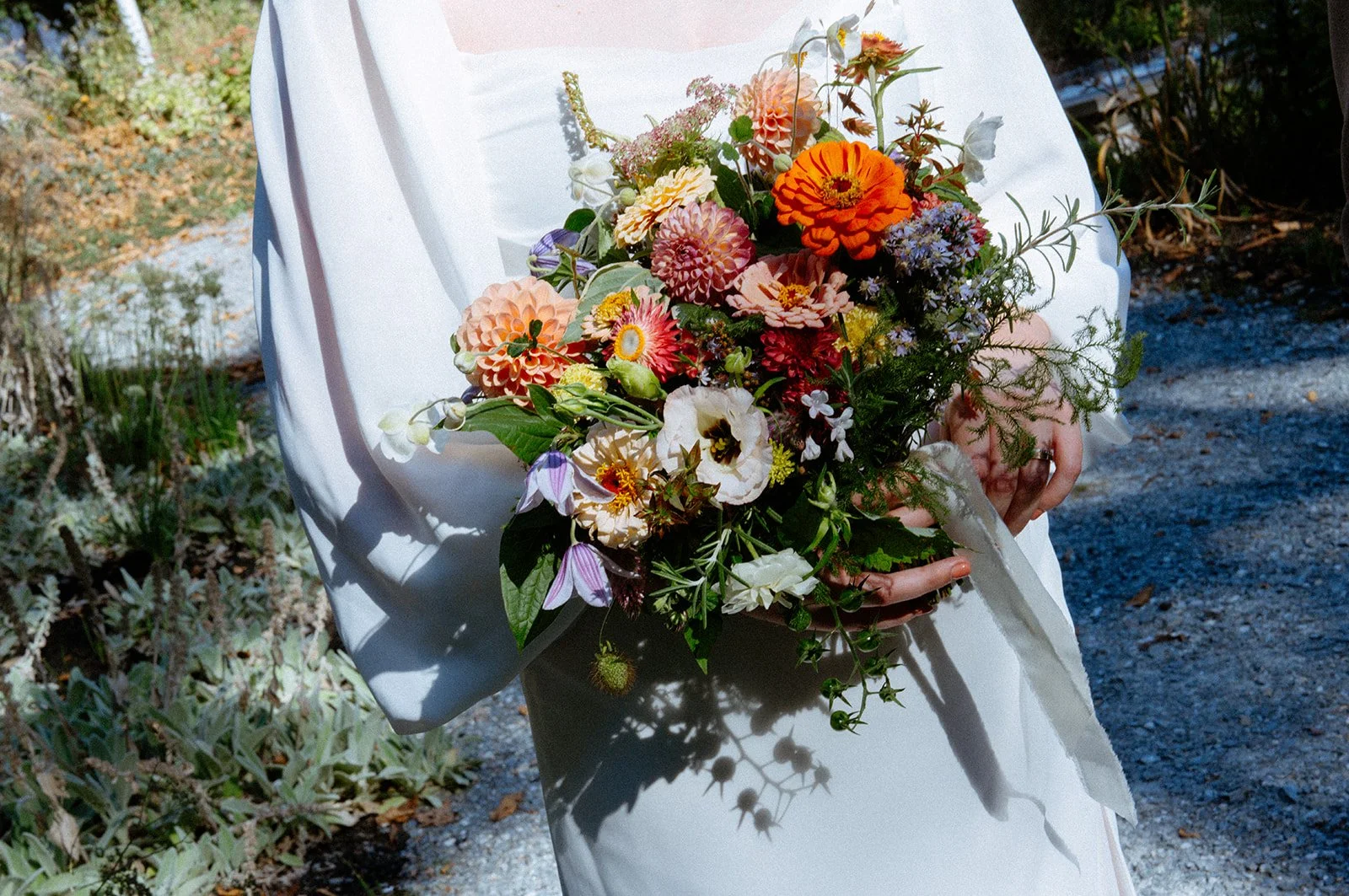Person in a white dress holding a colorful bouquet of flowers outdoors.