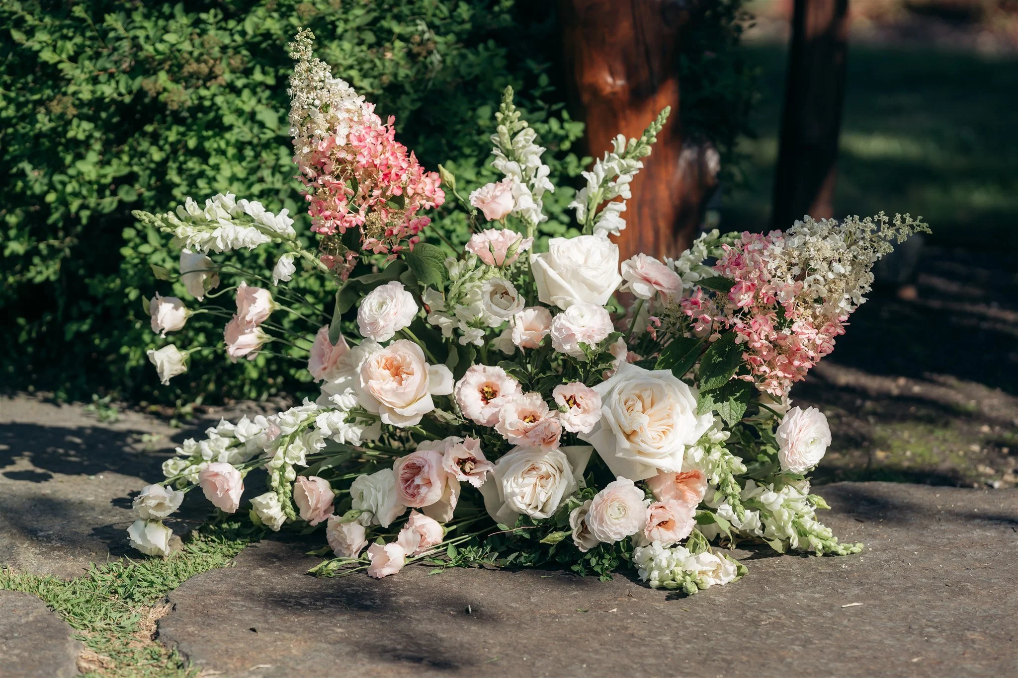 A floral arrangement with white and pink flowers on stone ground outdoors.
