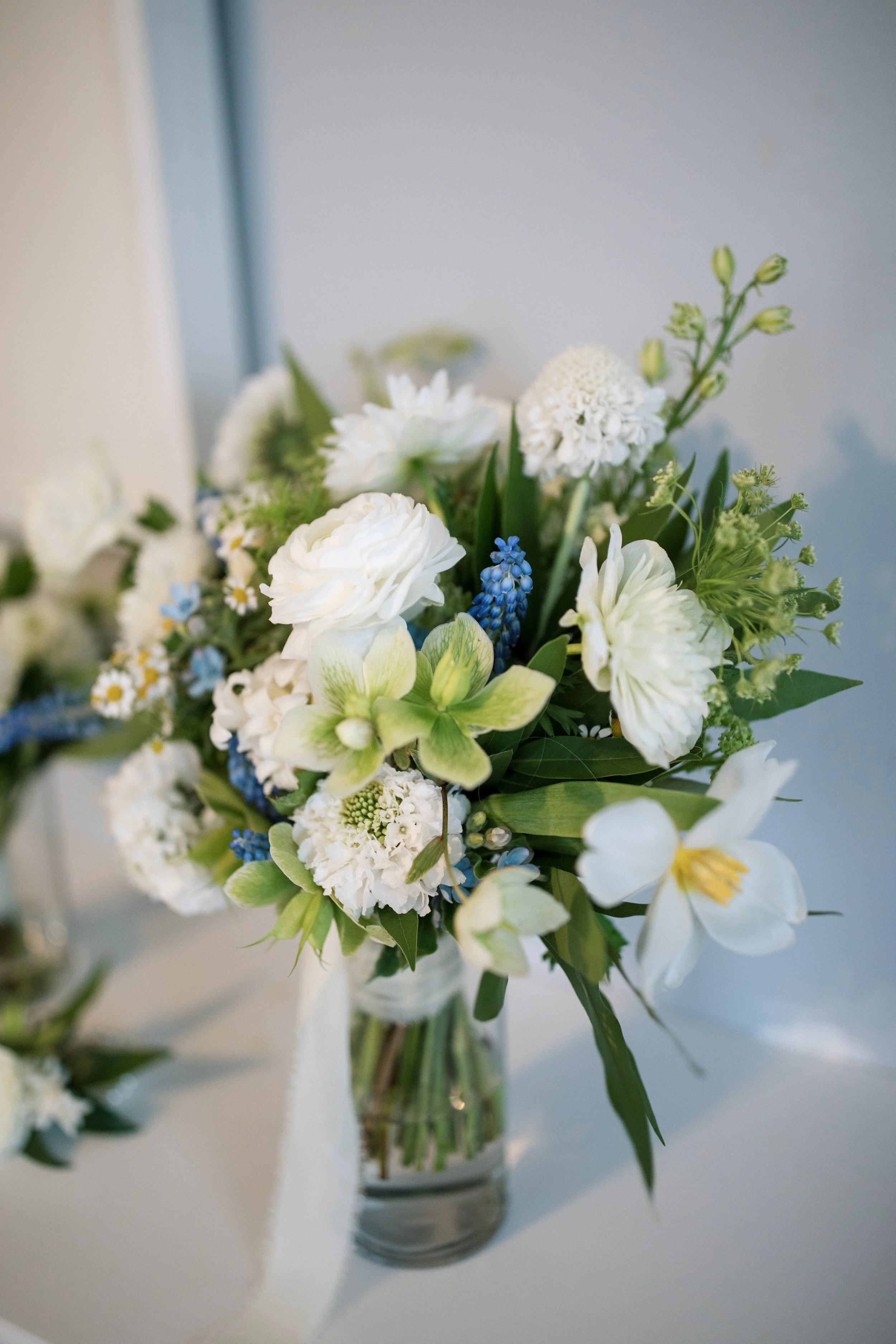 A bouquet of white, blue, and green flowers in a clear glass vase.