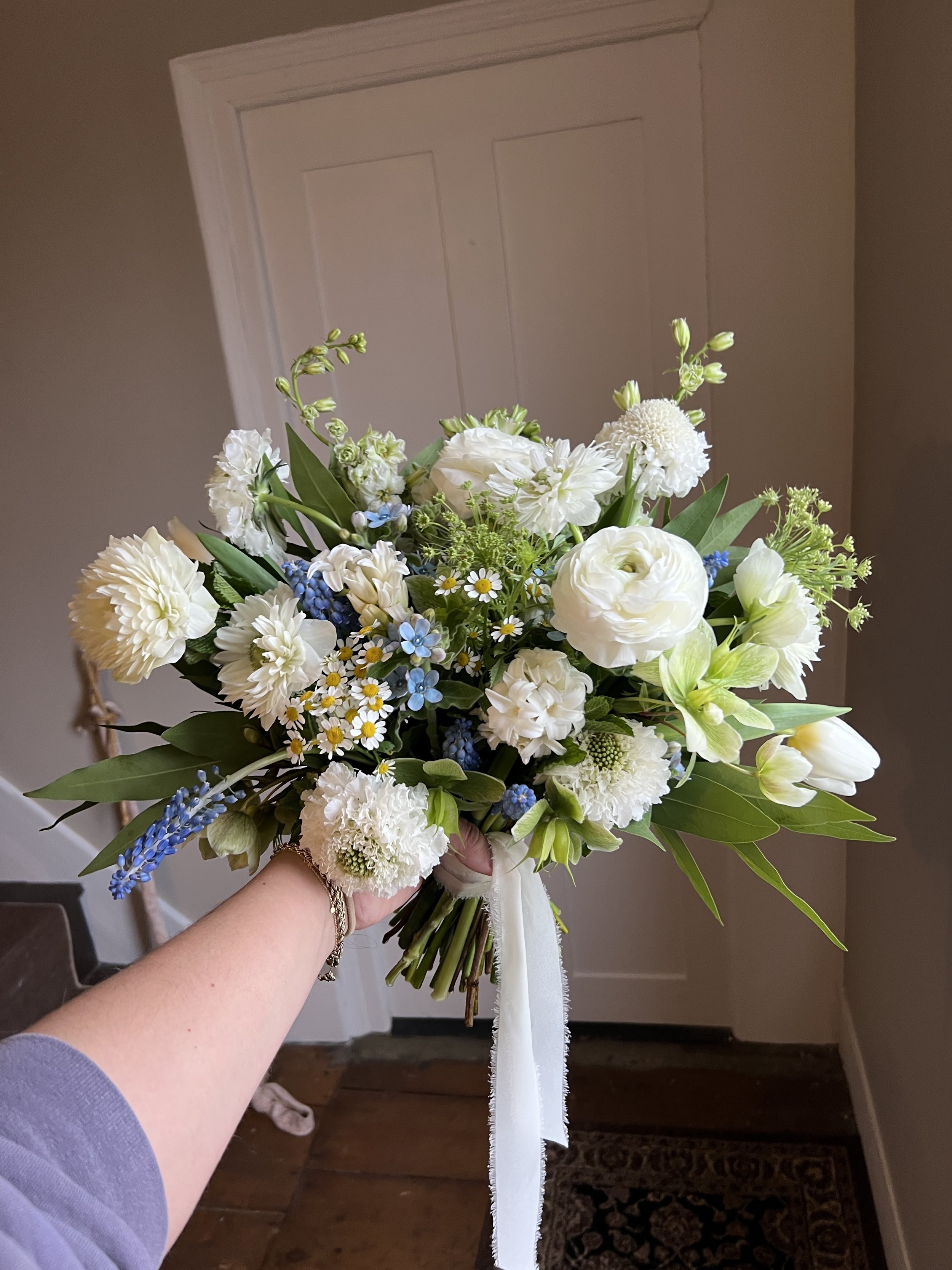 A person holding a bouquet of white and light blue flowers indoors.