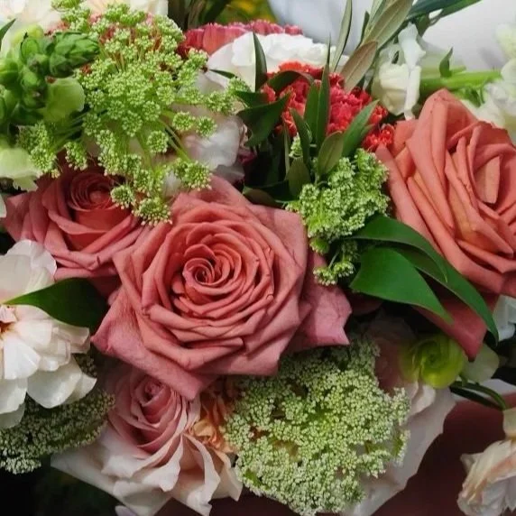 Close-up of a bouquet with pink roses, white and red flowers, and green foliage.