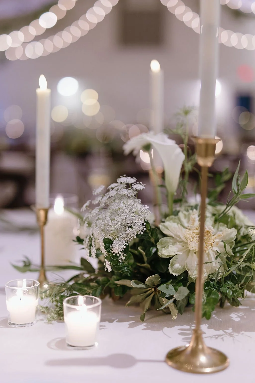 Elegant table centerpiece with white flowers, candles, and gold candle holders at a wedding or event.