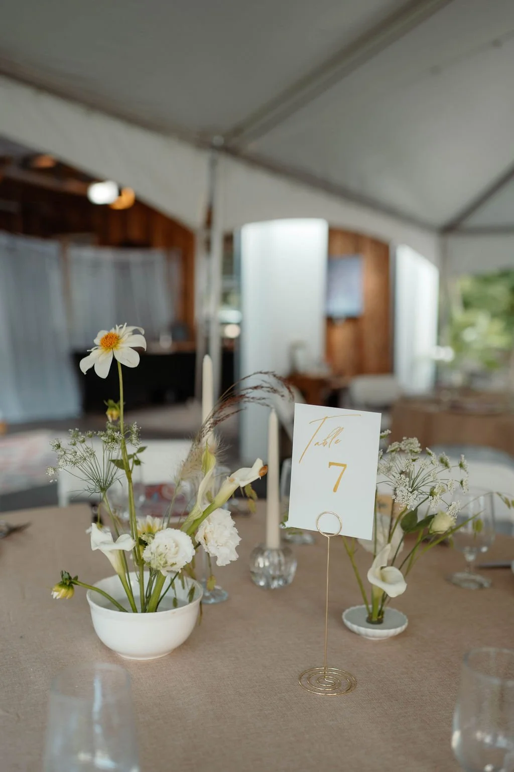 Table centerpiece with white flowers, candles, and a table number sign at an indoor event.