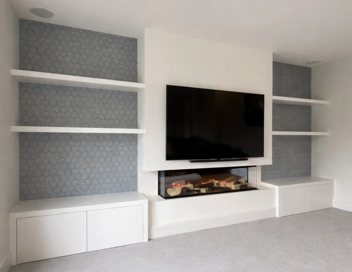 Living room with a mounted flat-screen TV above a modern electric fireplace, white built-in shelves