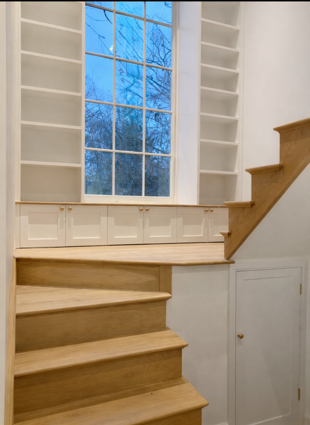 Solid oak staircase with low-level shaker cupboards, oak window seat and surrounding bookcases