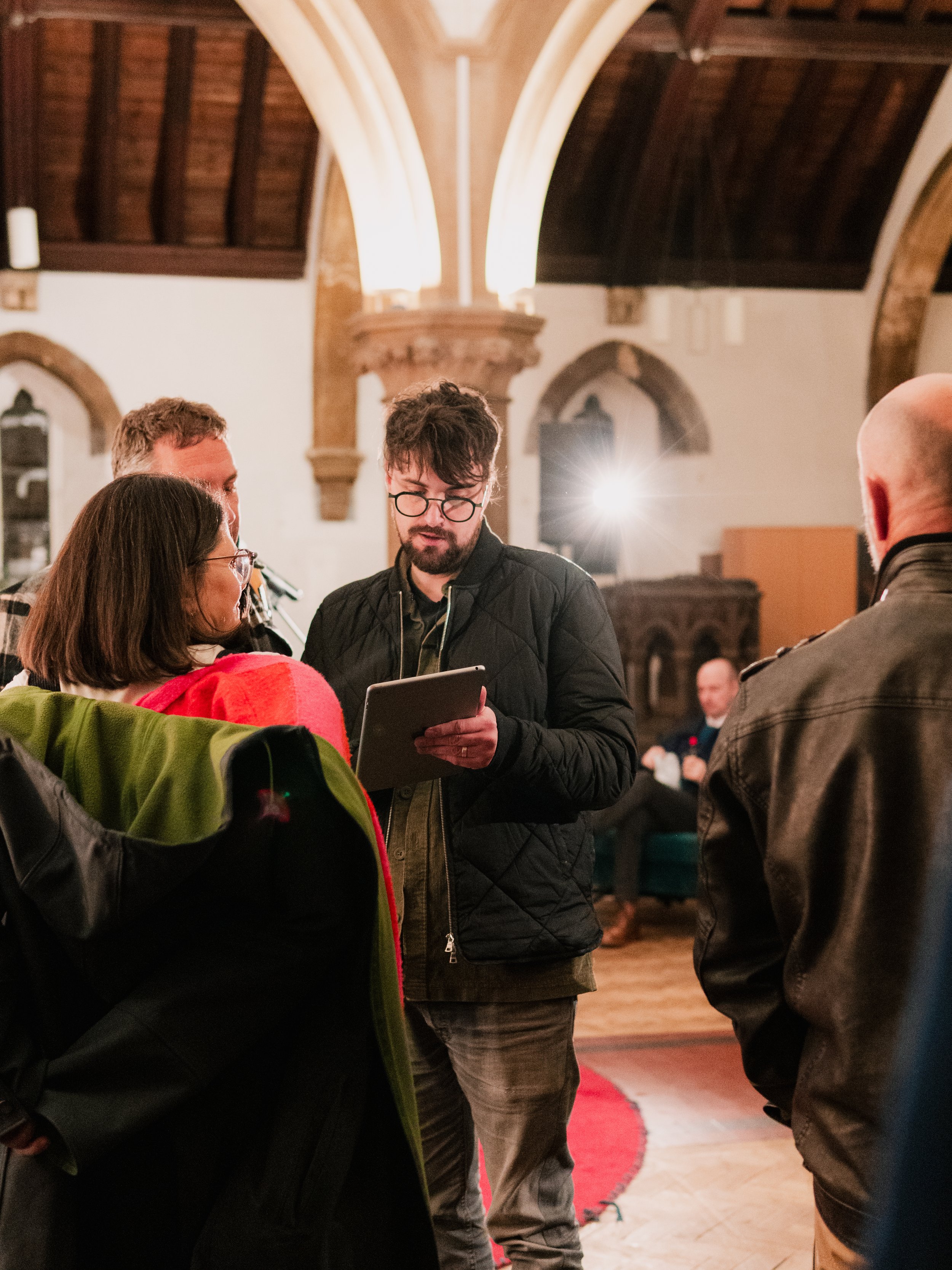 People gathered in a room with arched ceilings, one person holding a tablet.