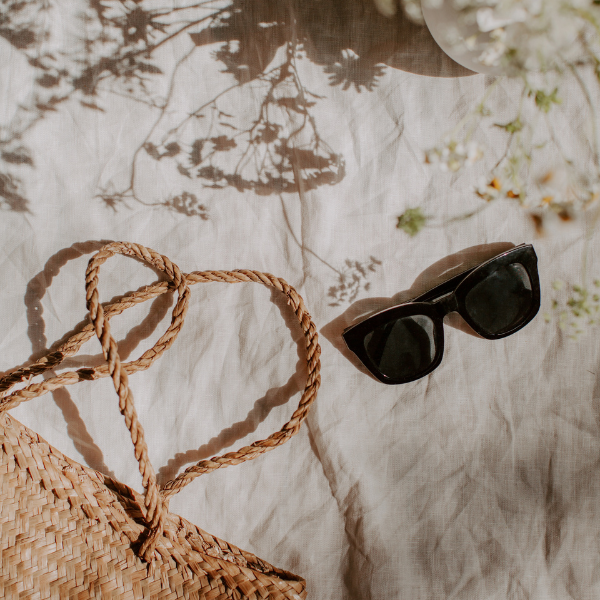 Korbtasche und Sonnenbrille auf hellem Leinenstoff, Sommer-Stillleben für einen entspannten Alltag