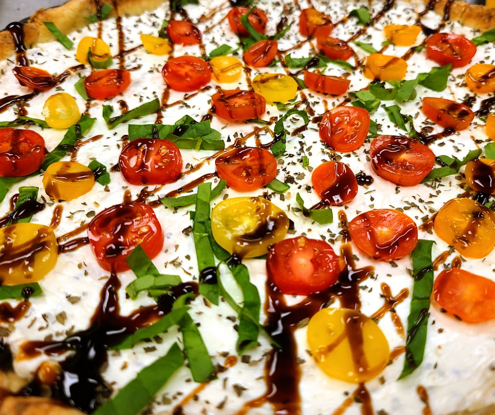 Caprese appetizer with cherry tomatoes, chopped green onions, drizzled balsamic glaze, and black pepper.