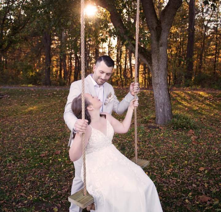 Bride and Groom on a swing in a wooded swing during sunset, with sunlight filtering through trees at an event venue.