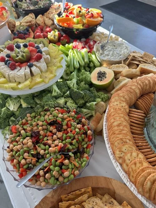 A charcuterie grazing table filled with a variety of snacks and fruits including vegetables, hummus, pita chips, cookies, fresh fruit, and a vegetable platter.