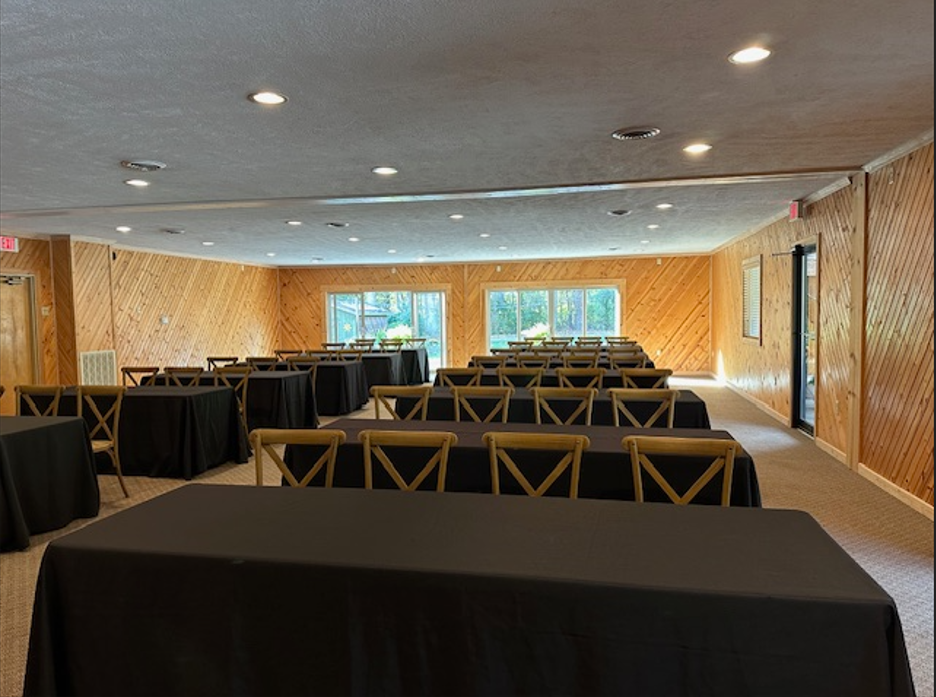 Corporate  conference room with black-covered tables, wooden chairs, and large windows showing outdoor trees.