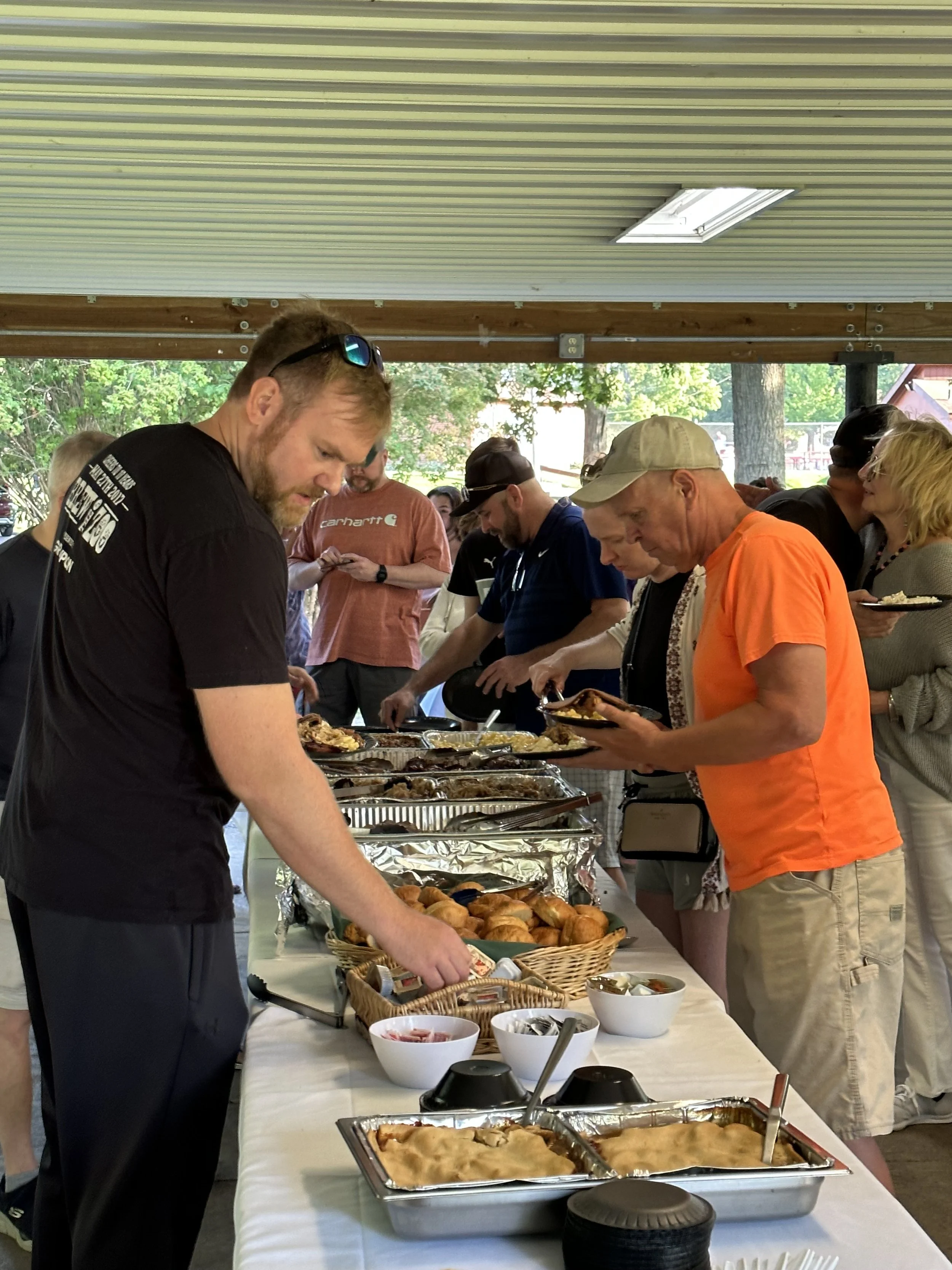 People serving themselves food at a buffet table with various dishes and bowls.