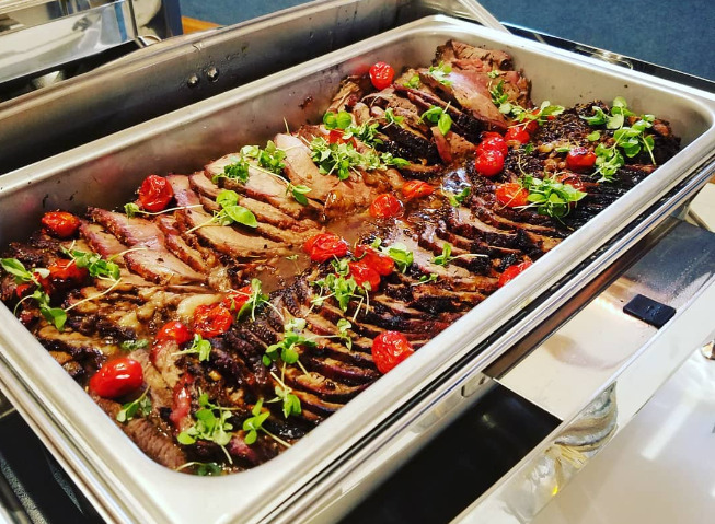 Sliced roasted beef garnished with cherry tomatoes and fresh herbs in a serving tray.