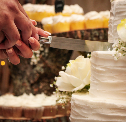 Person cutting a white wedding cake with a serrated knife.