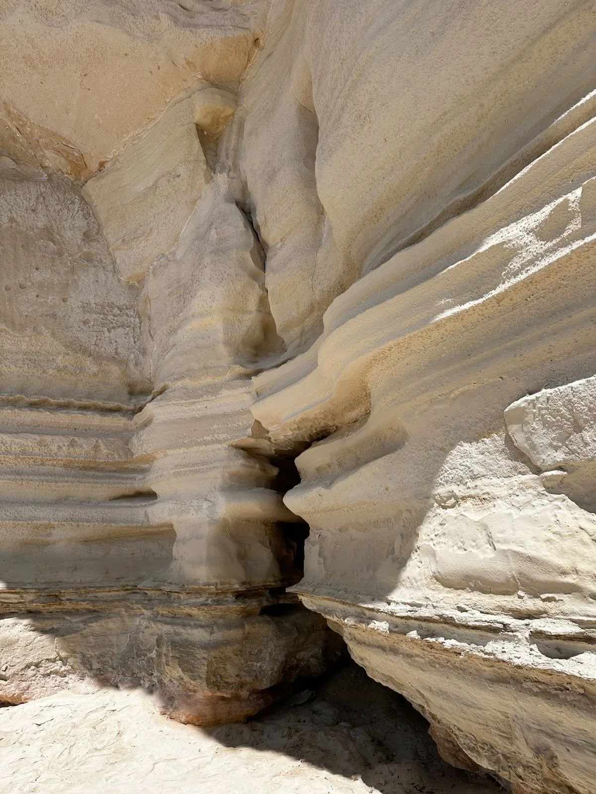 A photo of a sandy, rocky canyon with layered, eroded rock formations creating a deep crevice.